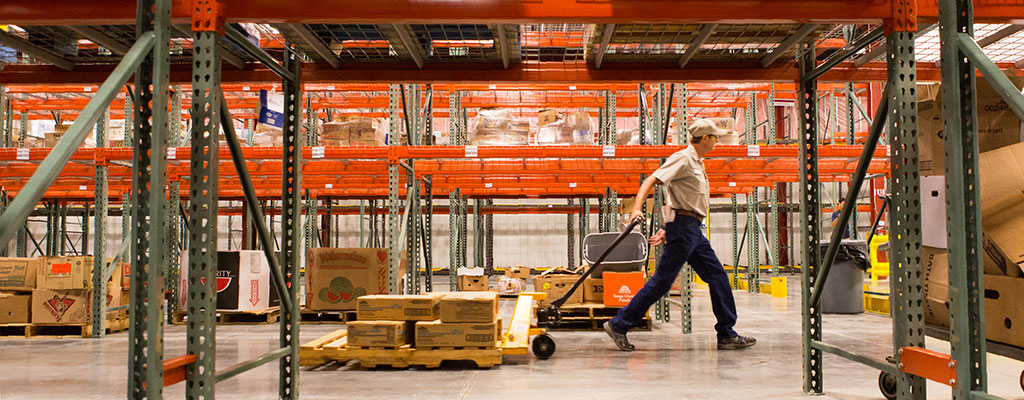 A Worker Moving Pallets Of Donated Food In A Warehouse